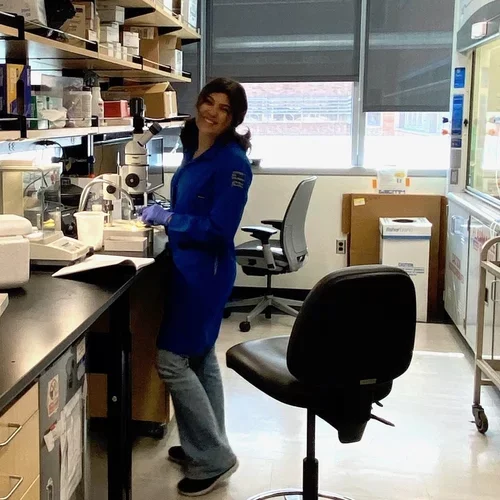 Priscilla wearing a lab coat and posing at a microscope on a lab bench at UCLA.