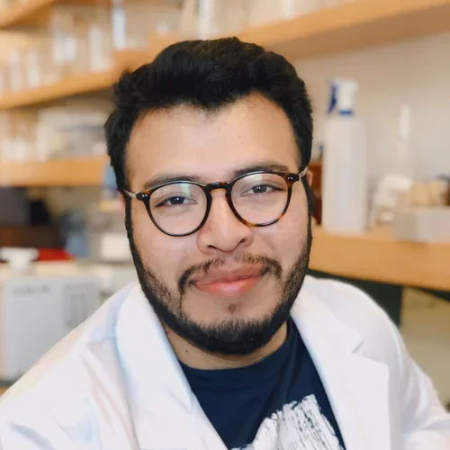 Portrait of Victor Mendoza wearing a lab coat in front of a laboratory wall.